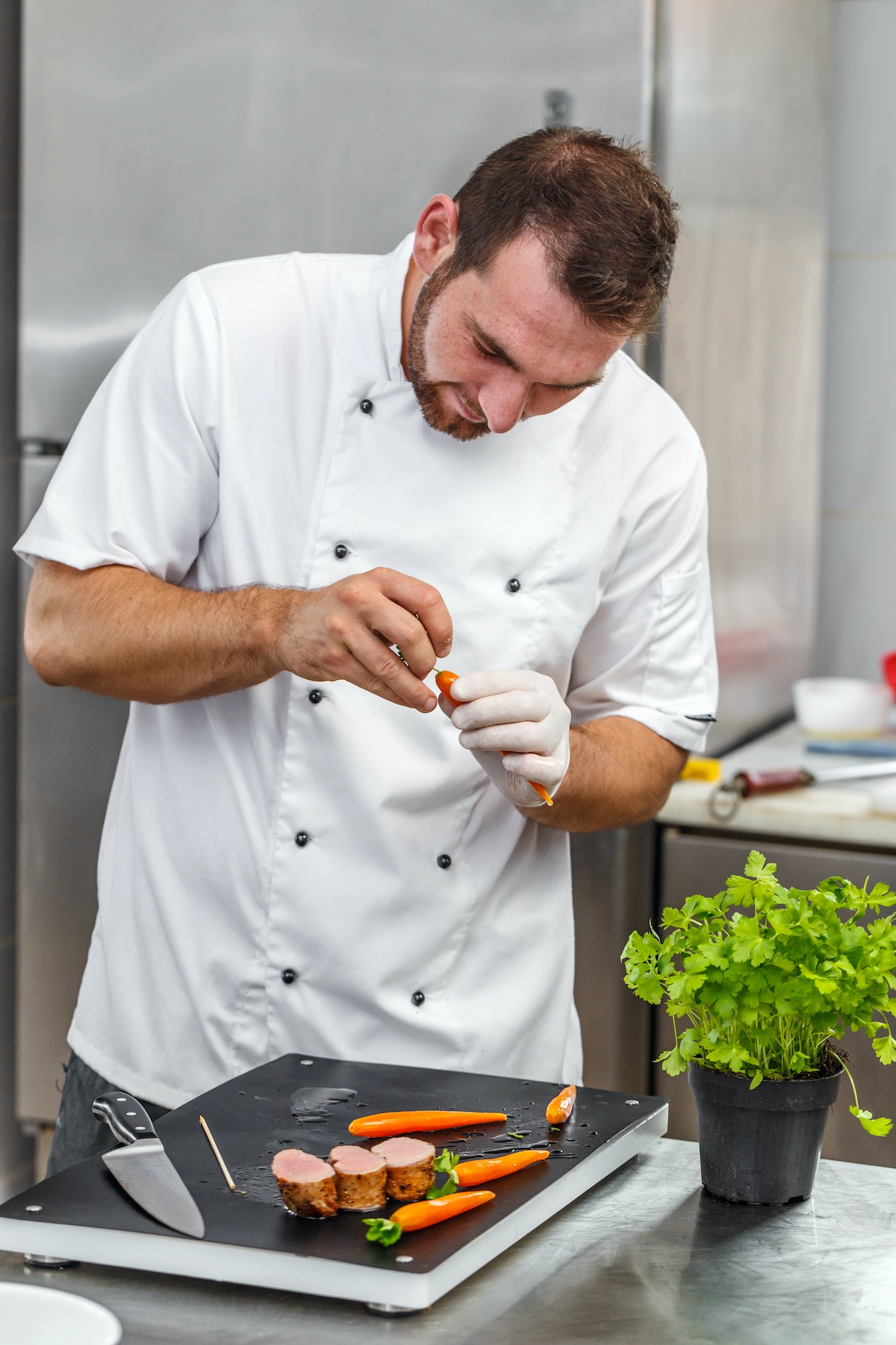 Chef preparing meat with carrots and parsley.