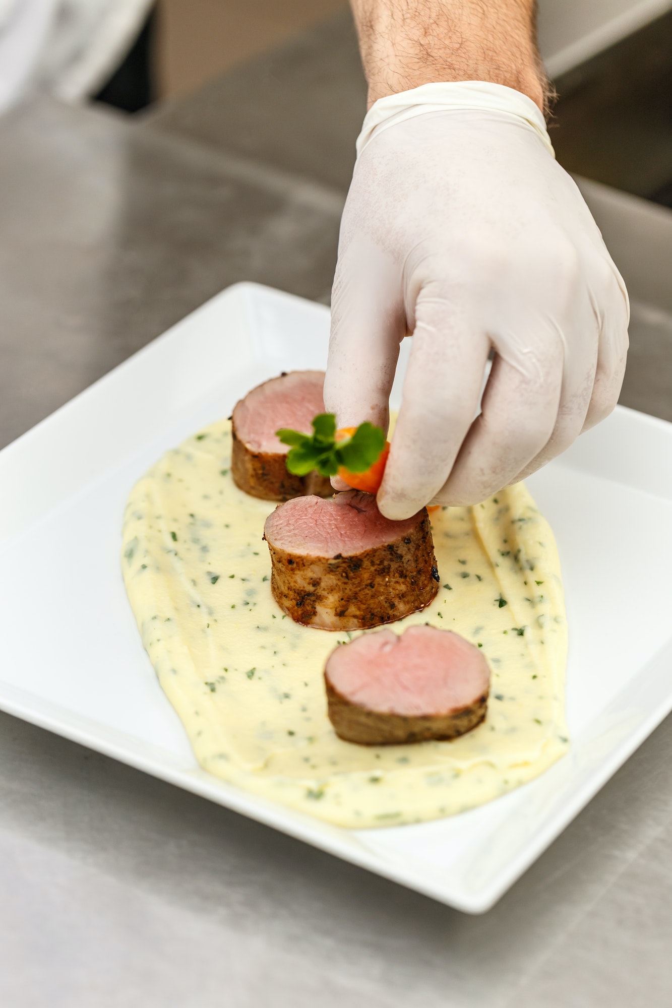 Hand plating mashed potatoes and meat.