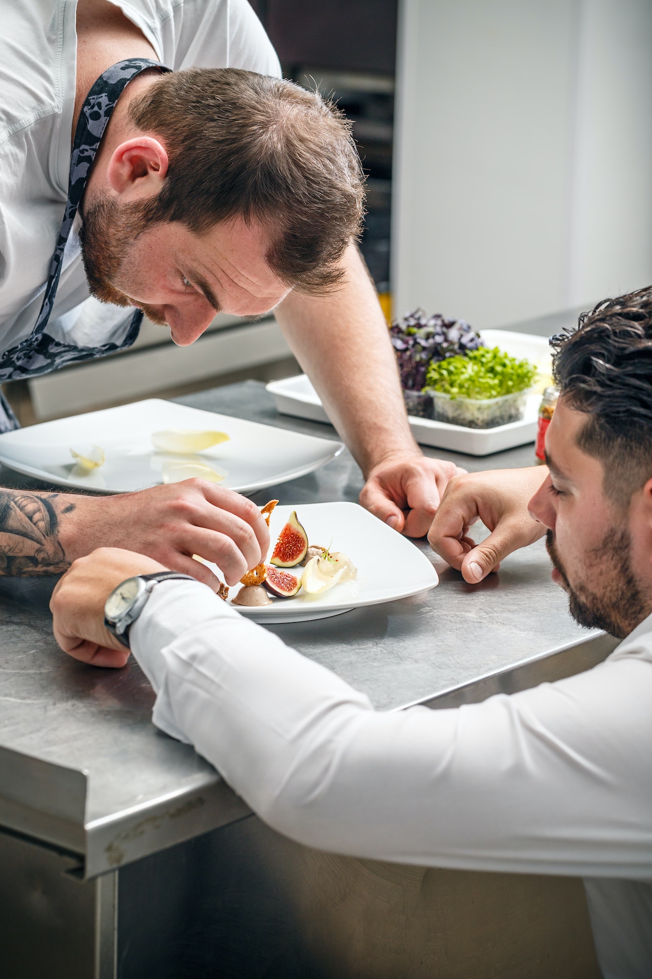 Two chefs plating fig and mousse dessert.